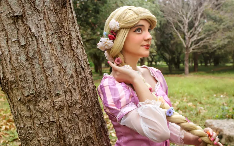 Rapunzel entre árboles, con su larga trenza decorada con flores